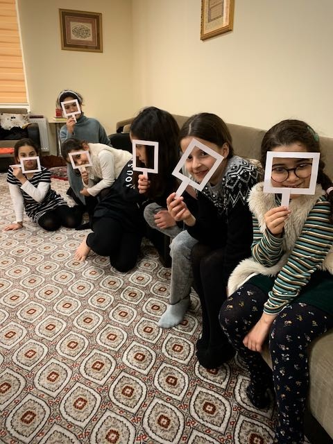 Girls holding paper frames in front of their faces during a photography exercise